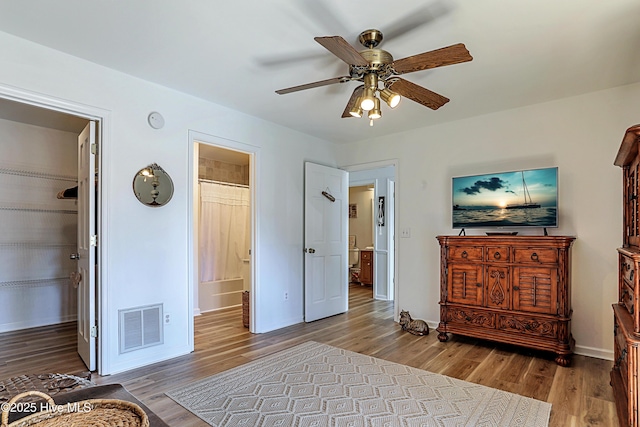 bedroom featuring visible vents, ensuite bathroom, wood finished floors, baseboards, and ceiling fan