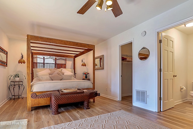 bedroom with a spacious closet, visible vents, baseboards, wood finished floors, and a ceiling fan