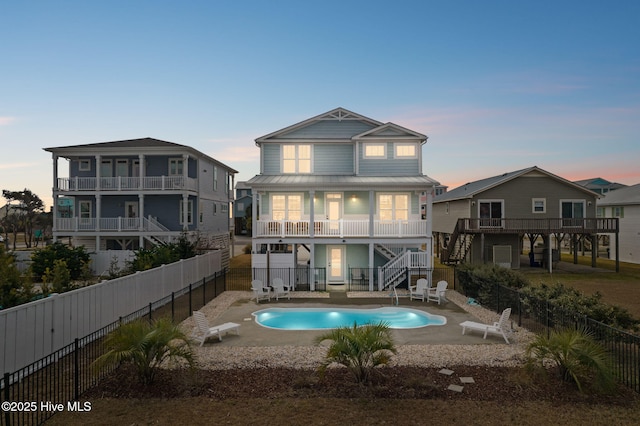 back house at dusk featuring a fenced in pool, a patio, and a balcony