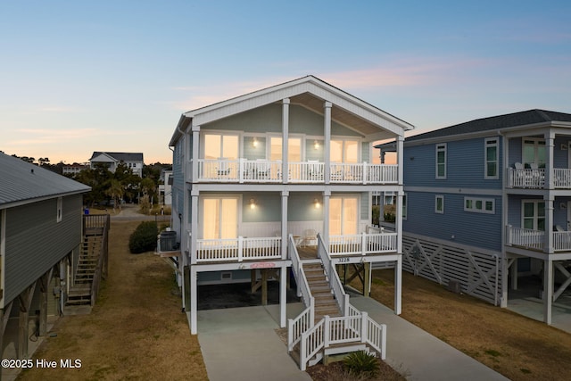 back house at dusk with a balcony, a porch, a yard, and central air condition unit