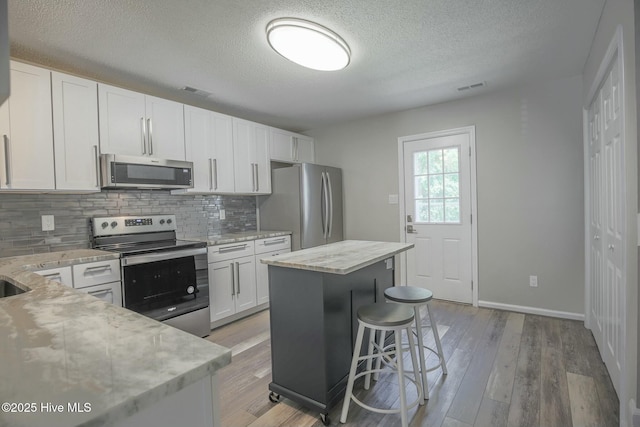 kitchen featuring white cabinetry, light stone counters, a center island, and appliances with stainless steel finishes