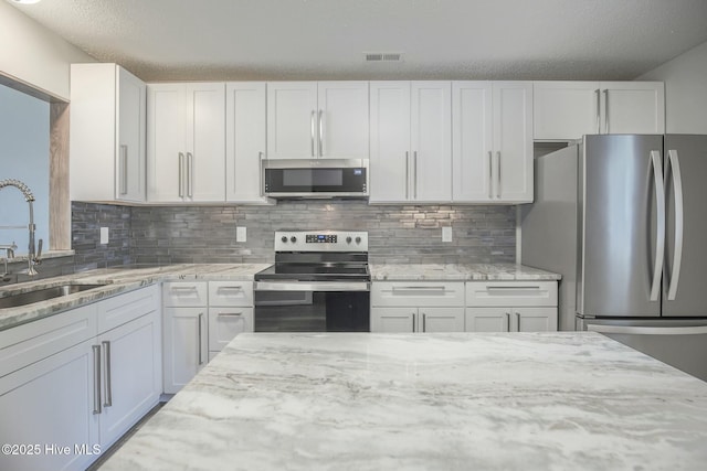 kitchen featuring sink, appliances with stainless steel finishes, white cabinetry, light stone counters, and tasteful backsplash