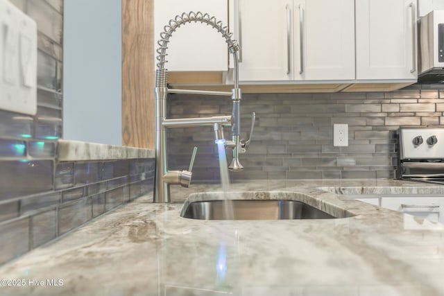 kitchen featuring sink, backsplash, white cabinets, and light stone counters