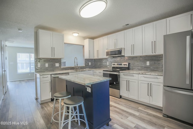 kitchen with sink, a kitchen island, stainless steel appliances, light stone countertops, and white cabinets