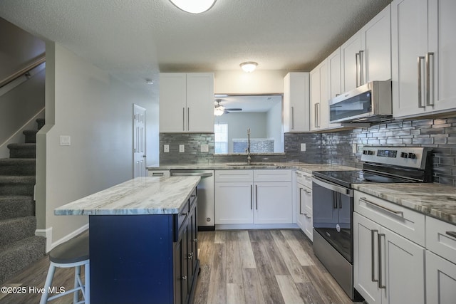 kitchen with sink, appliances with stainless steel finishes, a center island, light stone countertops, and white cabinets