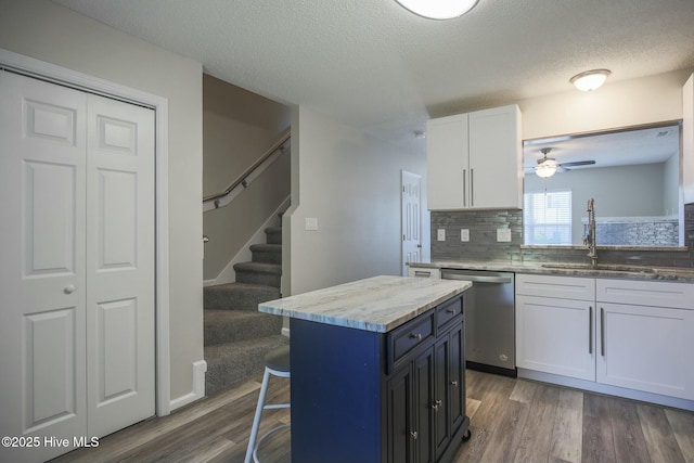 kitchen with sink, white cabinetry, light stone countertops, a kitchen island, and stainless steel dishwasher