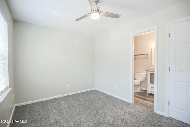 unfurnished bedroom featuring ceiling fan, ensuite bath, carpet floors, and multiple windows