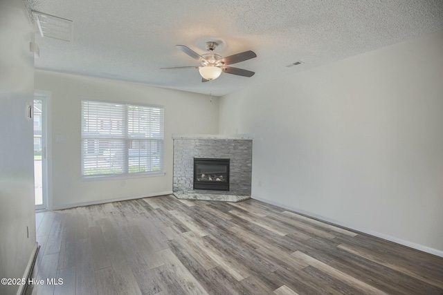 unfurnished living room featuring hardwood / wood-style flooring, ceiling fan, a stone fireplace, and a textured ceiling