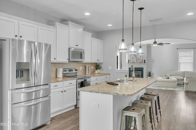 kitchen with a breakfast bar area, white cabinetry, appliances with stainless steel finishes, an island with sink, and pendant lighting