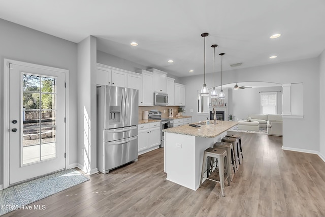 kitchen featuring white cabinetry, pendant lighting, stainless steel appliances, and an island with sink