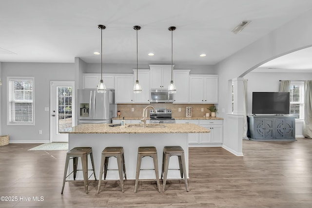 kitchen featuring stainless steel appliances, white cabinetry, a kitchen island with sink, and light stone counters