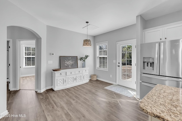 kitchen with stainless steel fridge, light stone countertops, white cabinets, decorative light fixtures, and light wood-type flooring