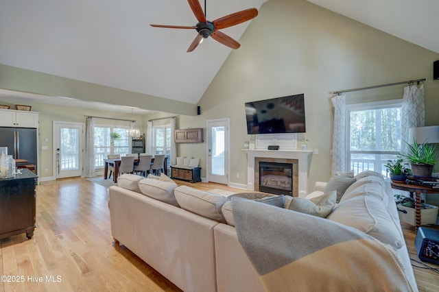 living room with a tile fireplace, a healthy amount of sunlight, high vaulted ceiling, and light hardwood / wood-style flooring