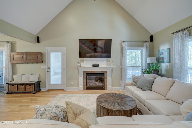 living room with high vaulted ceiling, a tile fireplace, and light wood-type flooring