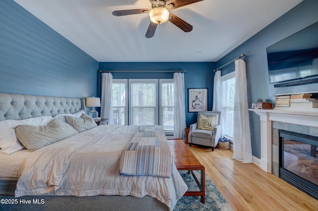 bedroom with ceiling fan, a fireplace, and light hardwood / wood-style flooring