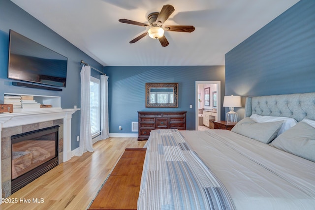 bedroom with ceiling fan, ensuite bathroom, a tiled fireplace, and light hardwood / wood-style floors