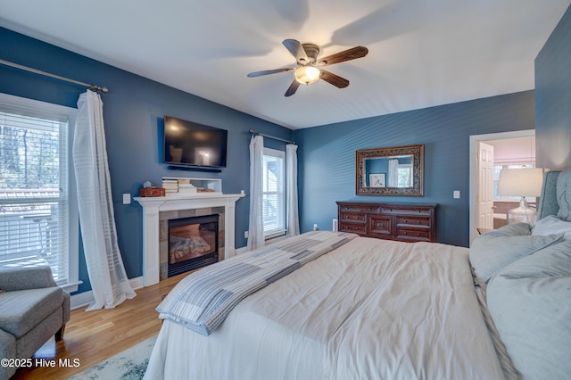 bedroom with a tiled fireplace, light hardwood / wood-style floors, and ceiling fan