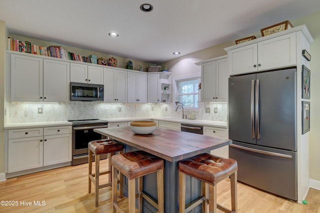 kitchen featuring appliances with stainless steel finishes, white cabinetry, butcher block counters, a kitchen breakfast bar, and light wood-type flooring