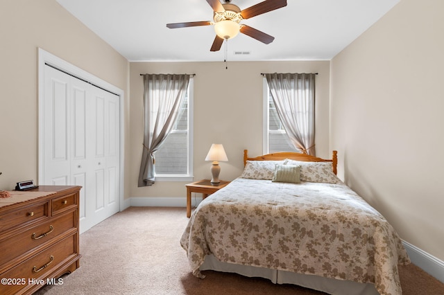 bedroom with multiple windows, light colored carpet, ceiling fan, and a closet