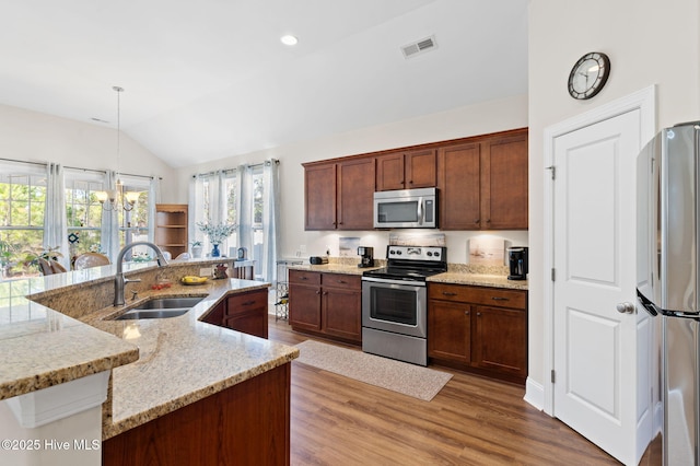 kitchen featuring vaulted ceiling, pendant lighting, sink, a kitchen island with sink, and stainless steel appliances