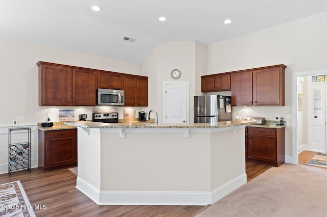 kitchen with light stone counters, stainless steel appliances, a kitchen bar, and a kitchen island with sink