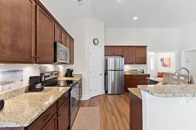 kitchen featuring sink, a center island with sink, light wood-type flooring, stainless steel appliances, and light stone countertops