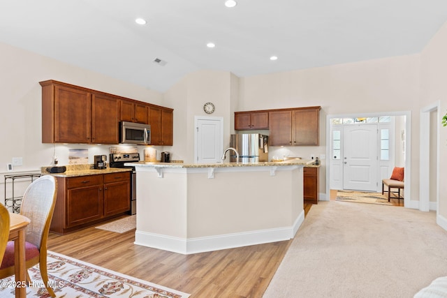 kitchen with light stone counters, appliances with stainless steel finishes, a breakfast bar, and a center island with sink