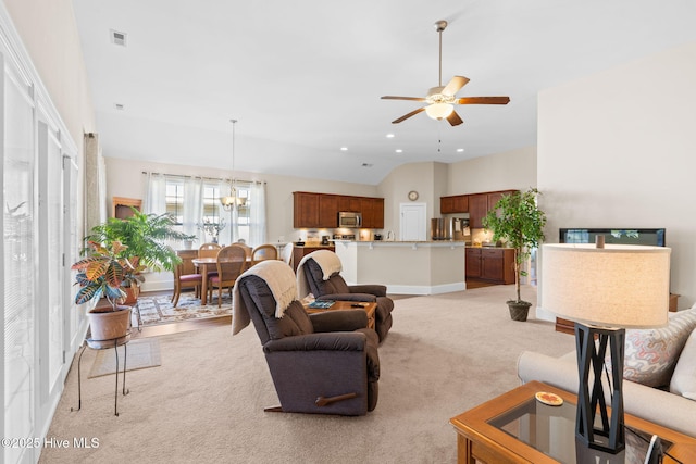 carpeted living room with ceiling fan with notable chandelier and vaulted ceiling