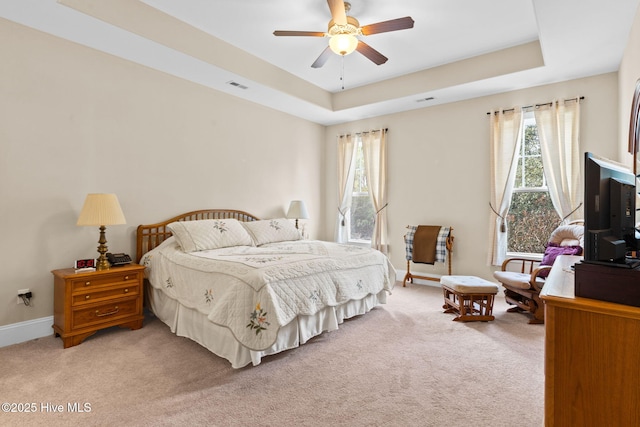 bedroom with light carpet, a tray ceiling, and ceiling fan