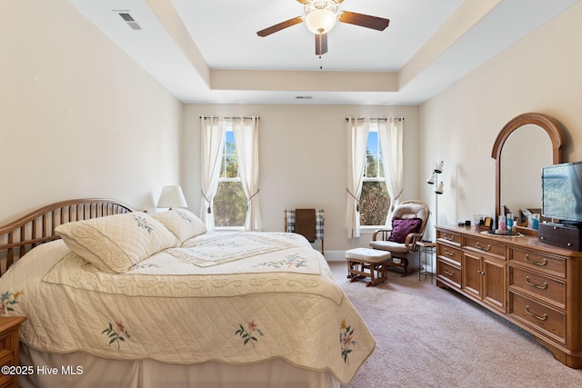 carpeted bedroom with ceiling fan and a tray ceiling