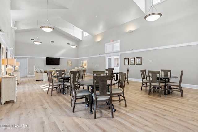 dining room with high vaulted ceiling and light hardwood / wood-style flooring