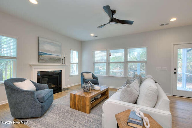 living room featuring recessed lighting, a fireplace with flush hearth, wood finished floors, baseboards, and visible vents