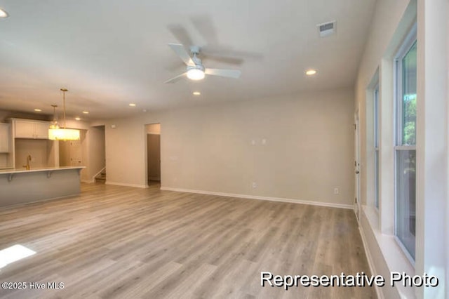 unfurnished living room featuring ceiling fan, sink, and light wood-type flooring