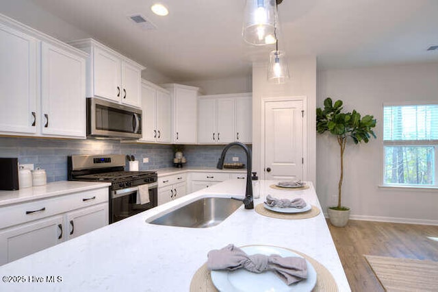 kitchen with tasteful backsplash, white cabinets, stainless steel appliances, light countertops, and a sink