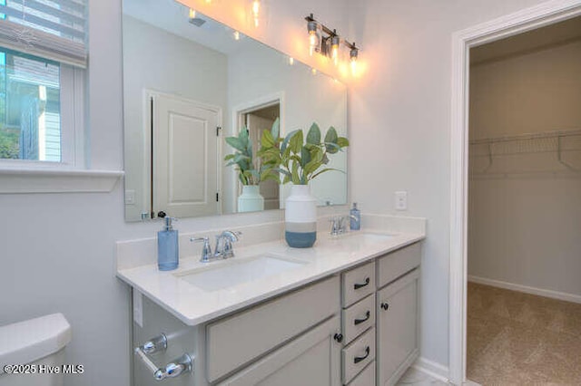 full bathroom featuring double vanity, a sink, toilet, and baseboards