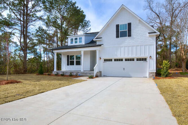 modern farmhouse style home with a garage, concrete driveway, covered porch, a front lawn, and board and batten siding