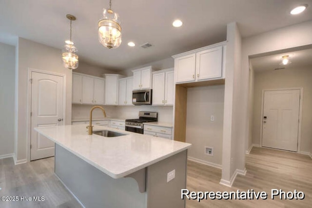 kitchen with sink, white cabinets, hanging light fixtures, a kitchen island with sink, and stainless steel appliances