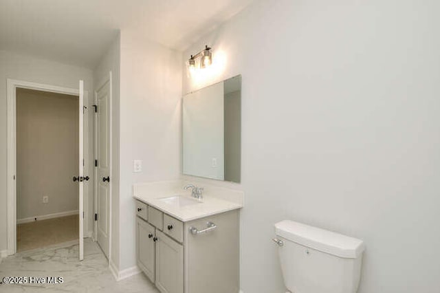 half bathroom with baseboards, vanity, and toilet