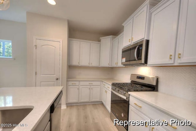 kitchen featuring stainless steel appliances, sink, white cabinets, and light wood-type flooring