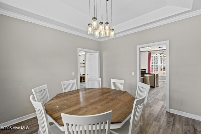 dining room with dark hardwood / wood-style flooring, ornamental molding, a raised ceiling, and an inviting chandelier