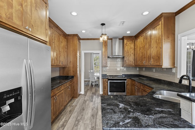 kitchen featuring sink, hanging light fixtures, appliances with stainless steel finishes, decorative backsplash, and wall chimney range hood