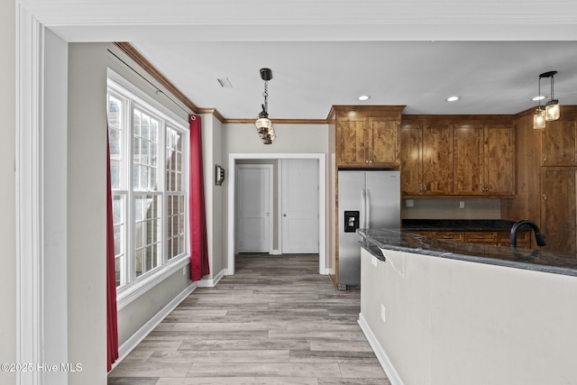 kitchen featuring dark stone counters, hanging light fixtures, ornamental molding, light hardwood / wood-style floors, and stainless steel fridge with ice dispenser