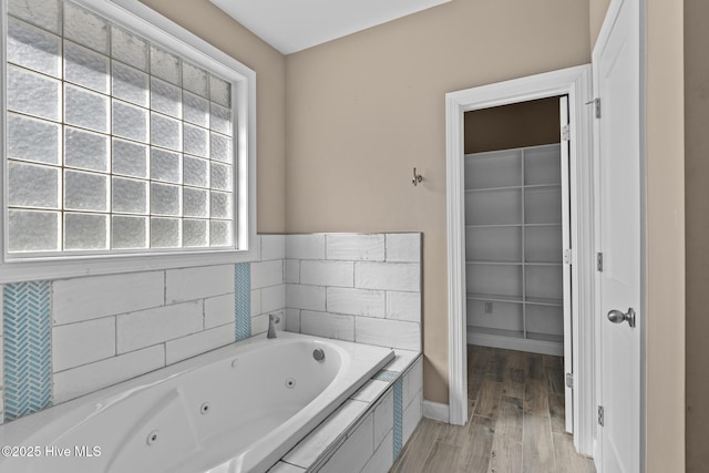 bathroom with tiled tub and wood-type flooring