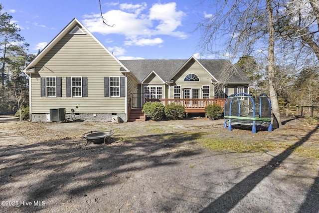 rear view of property featuring cooling unit, a deck, a fire pit, and a trampoline