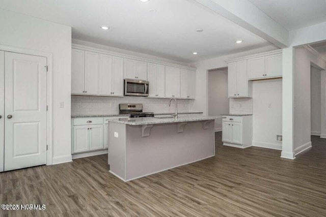 kitchen with dark wood-type flooring, appliances with stainless steel finishes, a kitchen island with sink, and white cabinets