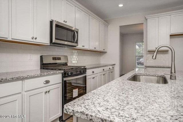 kitchen with stainless steel appliances, light stone countertops, sink, and white cabinets