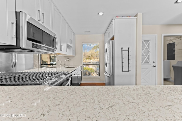 kitchen with stainless steel appliances, light stone countertops, sink, and white cabinets