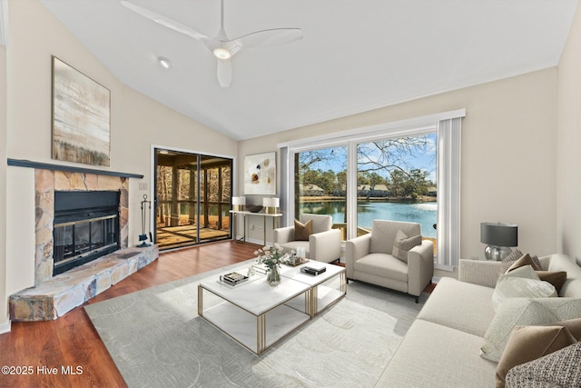 living room featuring a stone fireplace, a water view, vaulted ceiling, hardwood / wood-style flooring, and ceiling fan