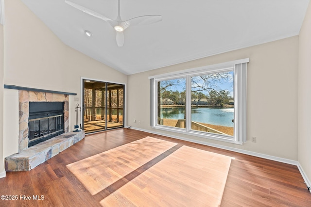 unfurnished living room featuring a water view, lofted ceiling, a stone fireplace, and hardwood / wood-style flooring