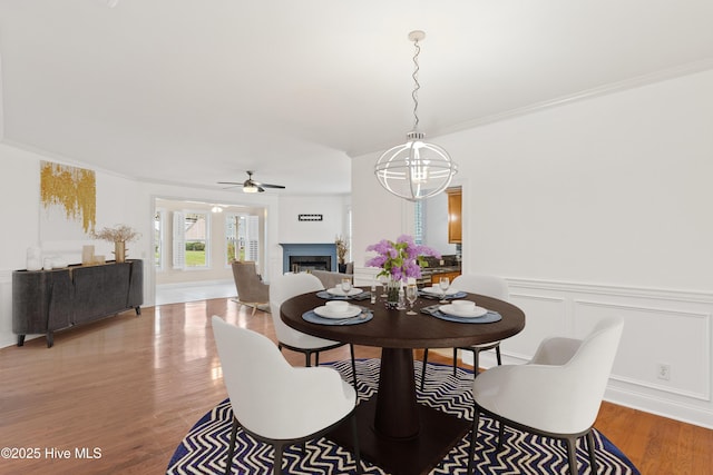 dining area with crown molding, wood-type flooring, and ceiling fan with notable chandelier